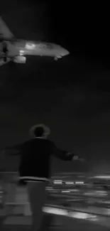 Person watches airplane flying overhead at night in a black and white scene.