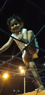 Child climbing playground ropes at night.