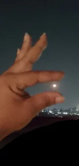 Hand framing the moon against a dark city night sky wallpaper.