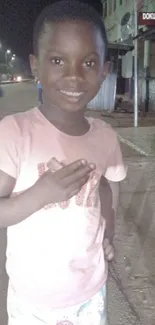 Child smiling on a dimly lit street at night.