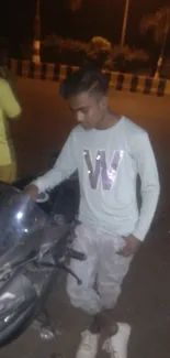 Young man in casual attire with a motorbike at night, urban street-style.