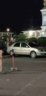 City street at night with a car parked near a monument.