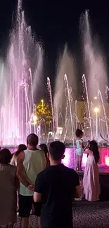 Nighttime fountain display with crowd and lights.