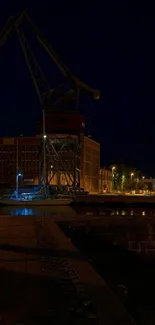 Nighttime harbor with crane silhouetted against a navy blue sky.