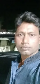 Nighttime portrait of person with car on street.