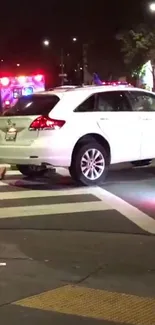 White SUV on a city street at night with ambulance lights glowing.