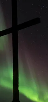 Silhouette of a cross against an aurora-lit night sky.