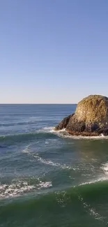 Serene ocean view with rock and blue sky.