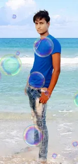 Young man in blue shirt on a beach with ocean and sky.