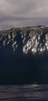 Sunlit ocean wave against a cloudy backdrop.