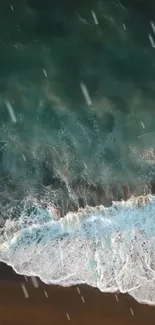 Aerial view of a teal ocean wave crashing on a sandy beach.