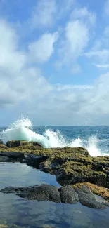 Ocean waves crash against a rocky shore under a blue cloudy sky.