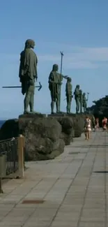 Statues by the ocean on a stone walkway with a clear blue sky.