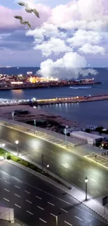 City coastline at night with ocean and clouds under a colorful sky.