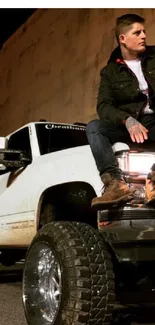 Man sitting on a lifted white truck with a rugged urban backdrop, perfect for adventure lovers.