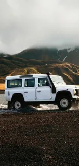 White SUV driving through rugged mountain terrain with cloudy sky.