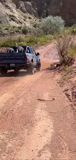 Blue truck driving on dusty off-road path with scenic background.