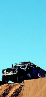 Off-road truck on desert dune under blue sky.