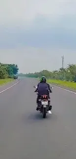 Motorcycle rider on an expansive open road with green landscapes and blue sky.