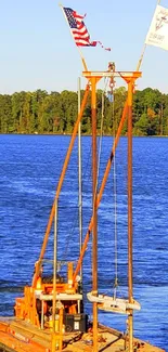 Orange barge floats on a blue lake with green trees in the background.