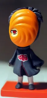 Anime figure with an orange spiral mask and black cloak standing.