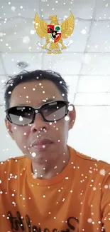 Man in sunglasses and orange shirt with snow effect on wallpaper.