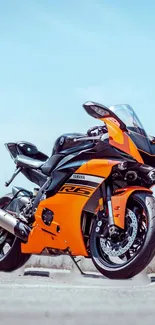 Orange and black sports bike on open road under blue sky.