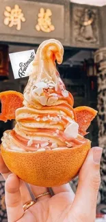 Orange swirl ice cream in orange shell with hand in exotic setting.