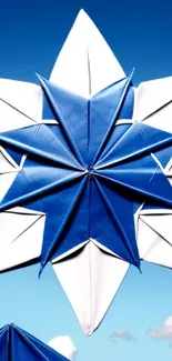 Blue and white origami star set against a clear, cloud-dotted blue sky.