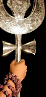 Silver trident held by hand with rosary on black background.