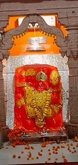 Vibrant orange temple deity with floral garlands in a carved alcove.