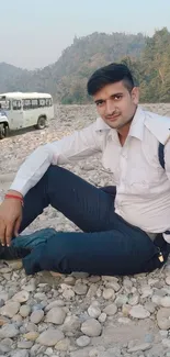 Man sitting on rocky terrain with a jeep in the background.