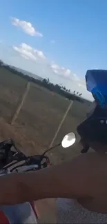 A person wearing a helmet riding a motorbike in a countryside setting under clear skies.