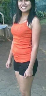 Person in orange top and black shorts smiling outside.