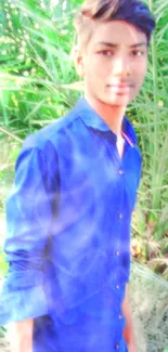 Young man in blue shirt outdoors with green foliage background.