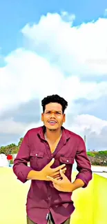 Man in maroon shirt stands outdoors against a bright, cloudy sky.