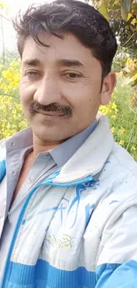 Man posing outdoors with floral and leafy background.