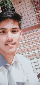 Young person in uniform smiling outdoors with a metal fence background.