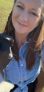 Woman smiling outdoors, holding camera, in sunlight with green background.