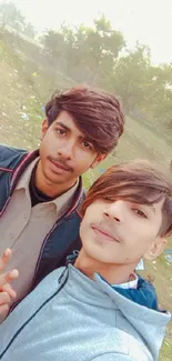 Two friends taking a selfie outdoors with greenery.