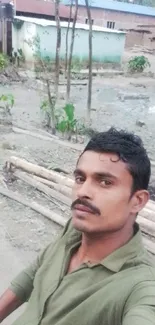 Selfie of a man in green shirt outdoors with rustic background.