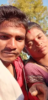 Outdoor selfie of a duo with blue sky and greenery in the background.