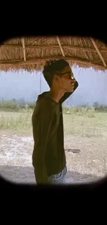 Person in sunglasses under a rustic shade outdoors.