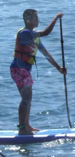 Person paddleboarding on a blue ocean with bright attire.