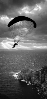 Paraglider silhouette against coast and dramatic sky.