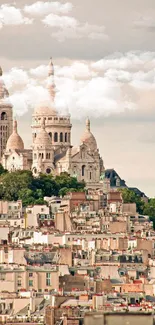 Paris skyline featuring Sacré-Cœur with rooftops in foreground, set against clouds.