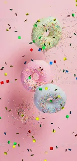 Three pastel donuts with sprinkles on pink background.