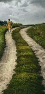 A lone figure walks on a winding path through lush green fields under a cloudy sky.