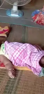 Baby sleeping on mat with pink blanket.