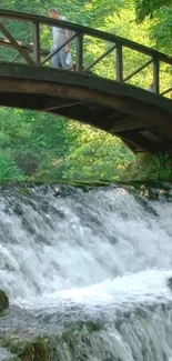 Wooden bridge over a cascading waterfall in a lush green forest.